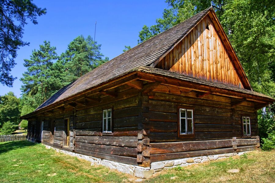 Log cabin with a steep timber roof under old oaks